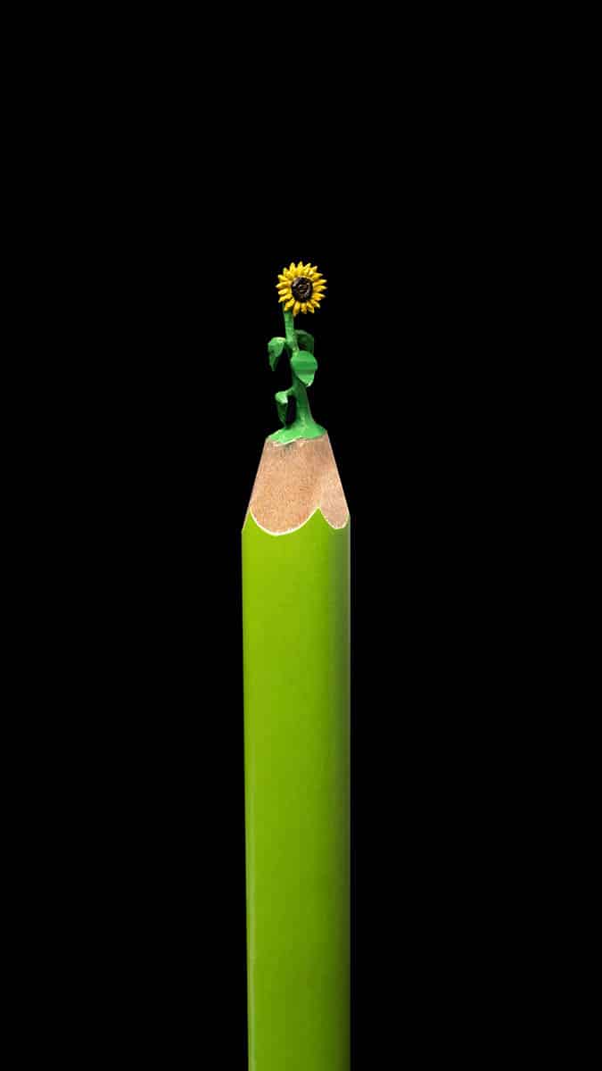Micro-sculpture of yellow sunflower and green stalk on the tip of a green colored pencil, by artist Salavat Fidai