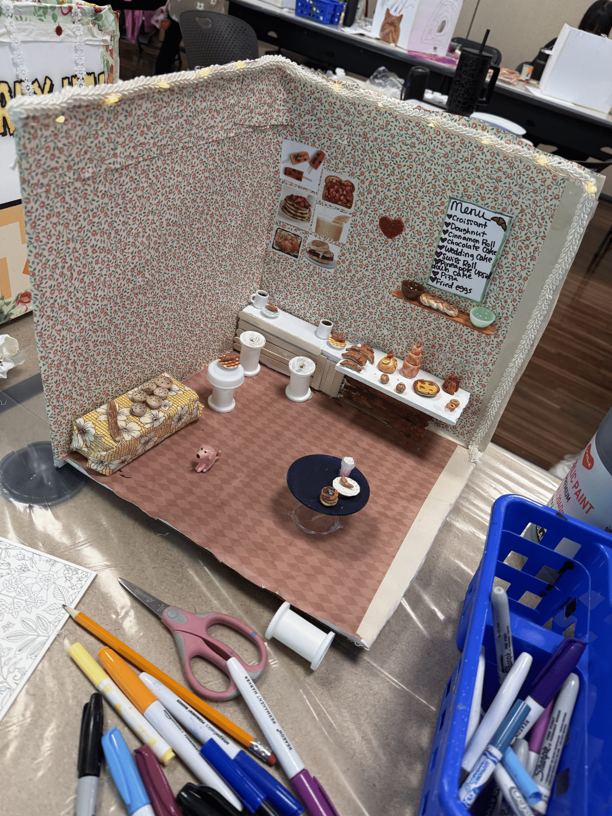 Miniature bakery diorama with pastry shelves, floral wallpaper, and a handwritten menu on the wall.