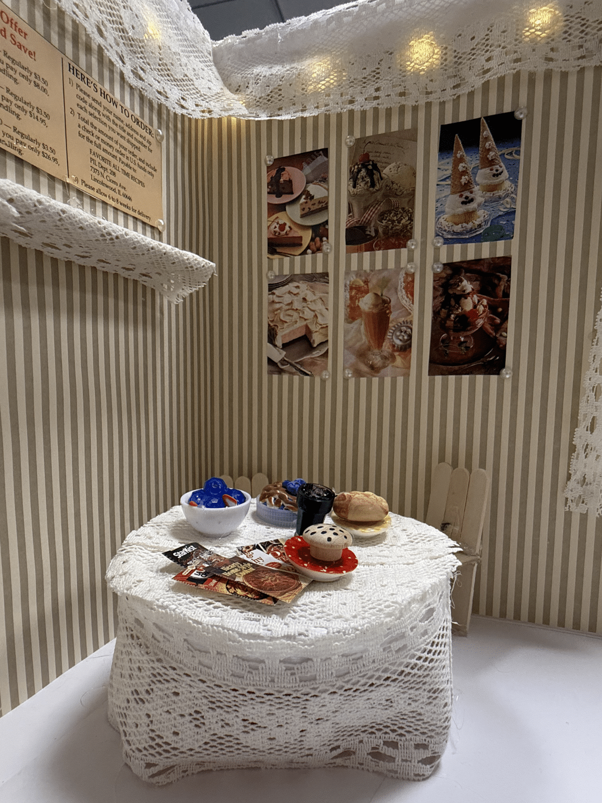 Small miniature dessert table with lace cloth, pastries, and wall photos in a striped-wall cafe scene