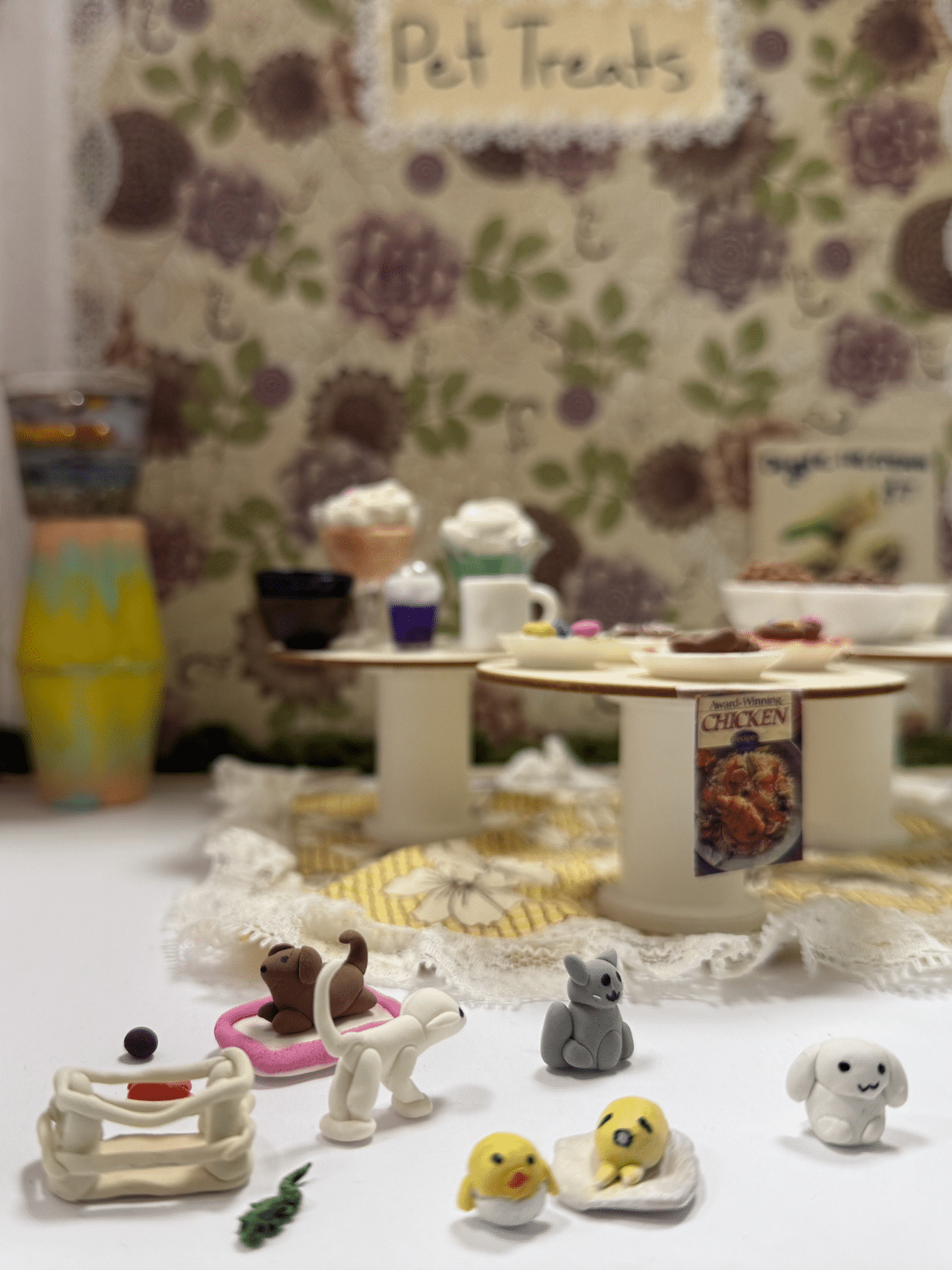 Pet-themed dessert table with mini clay animals in the foreground and treats on elevated stands against a floral backdrop labeled 'Pet Treats' in the background.